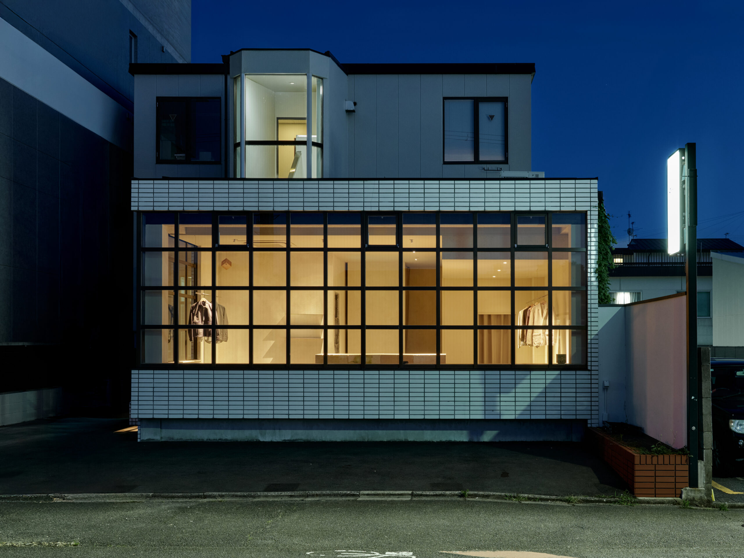 DSCF9324re 1 - 伊串工務店株式会社 Night-time exterior of a modern building with a large glass storefront showing clothing inside.