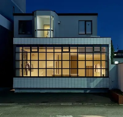 Night exterior of a modern storefront with large glass windows displaying mannequins inside a lit showroom.